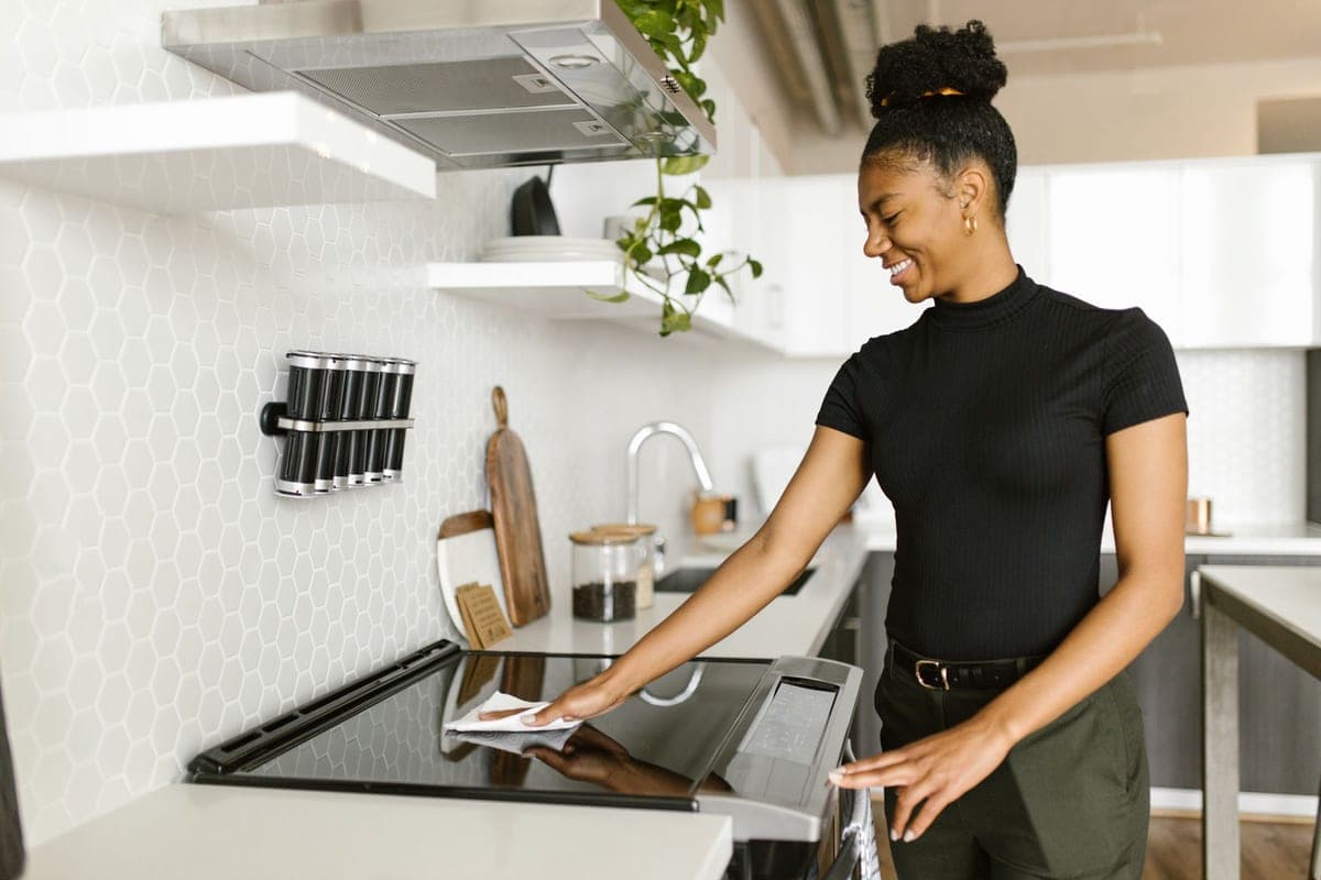 A smiling young woman wiping down a kitchen hob