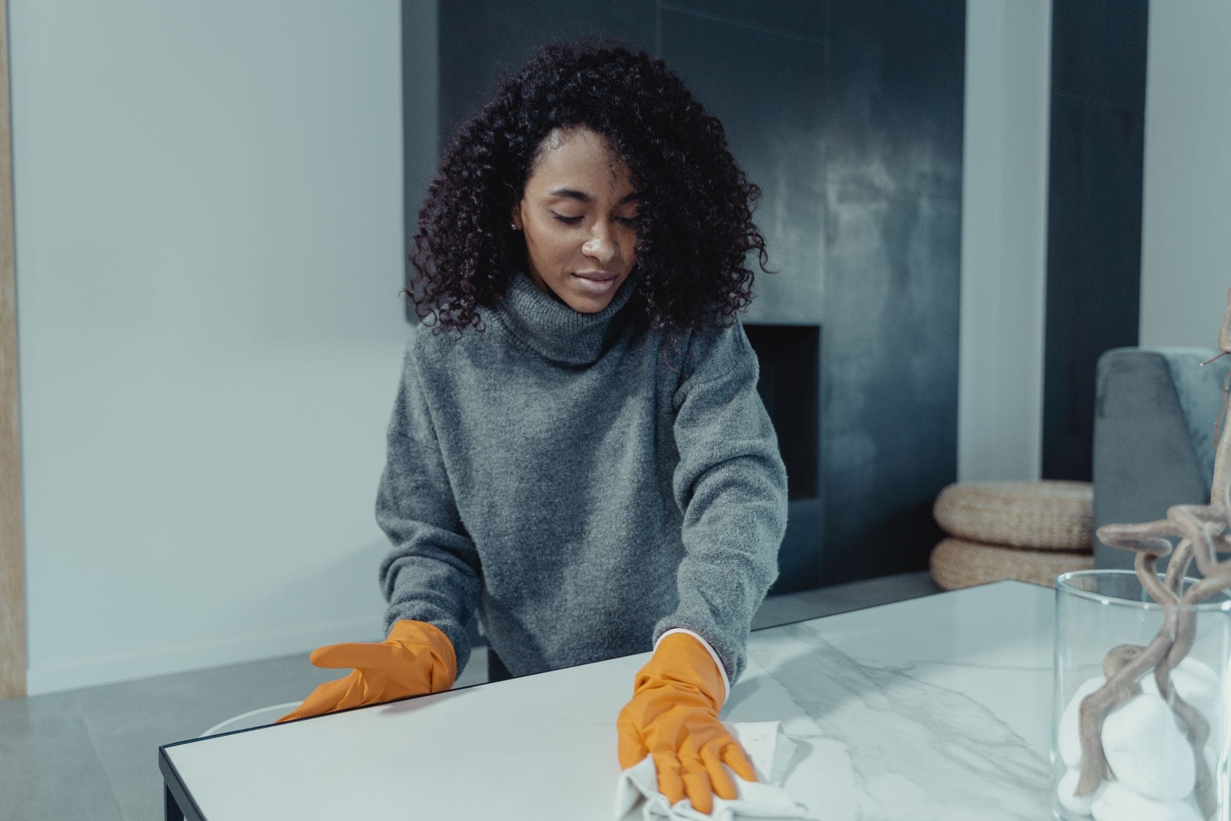 A young woman in rubber gloves wiping down a table in a bright, modern room