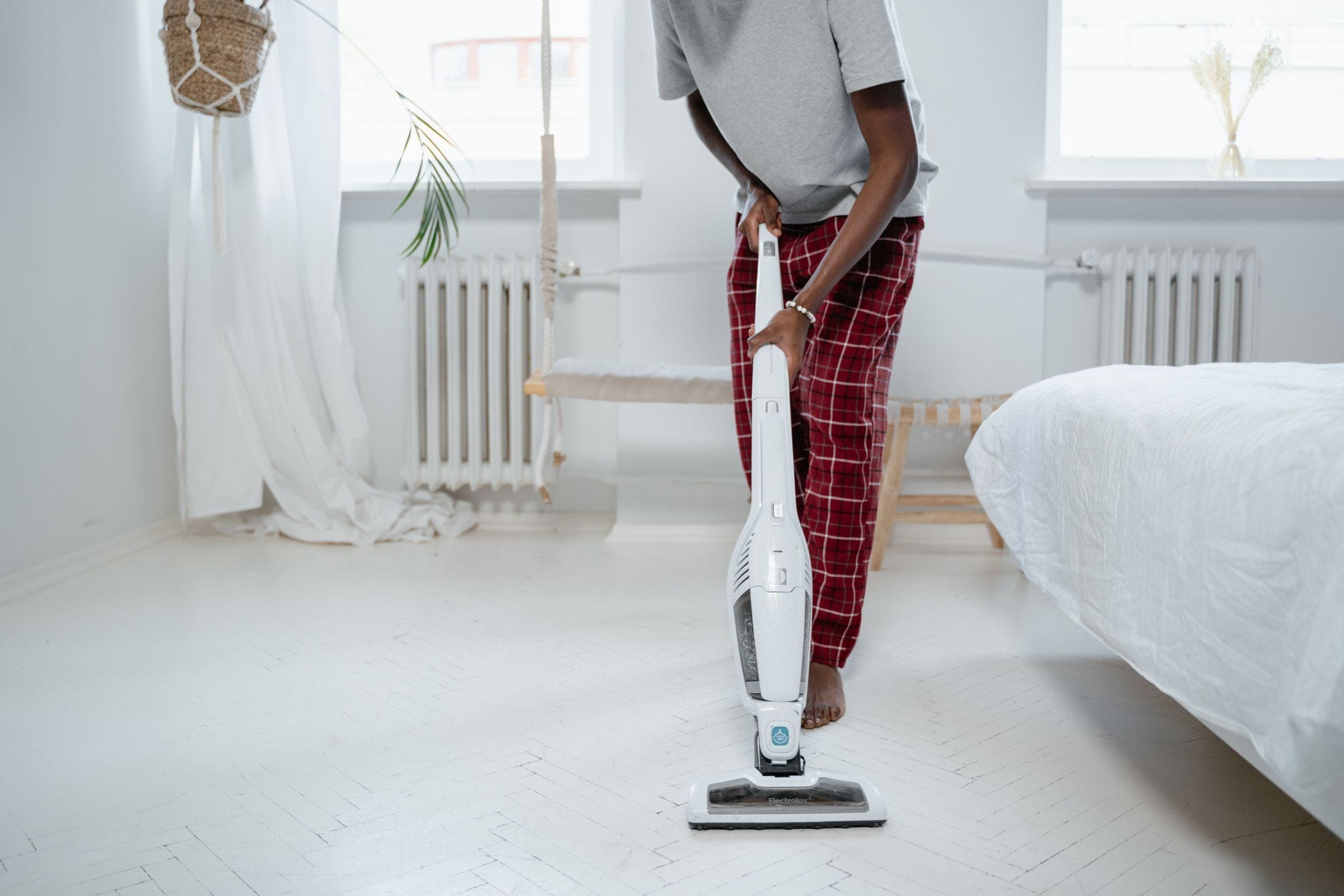 A volunteer vacuuming the floor of a bright, tidy bedroom