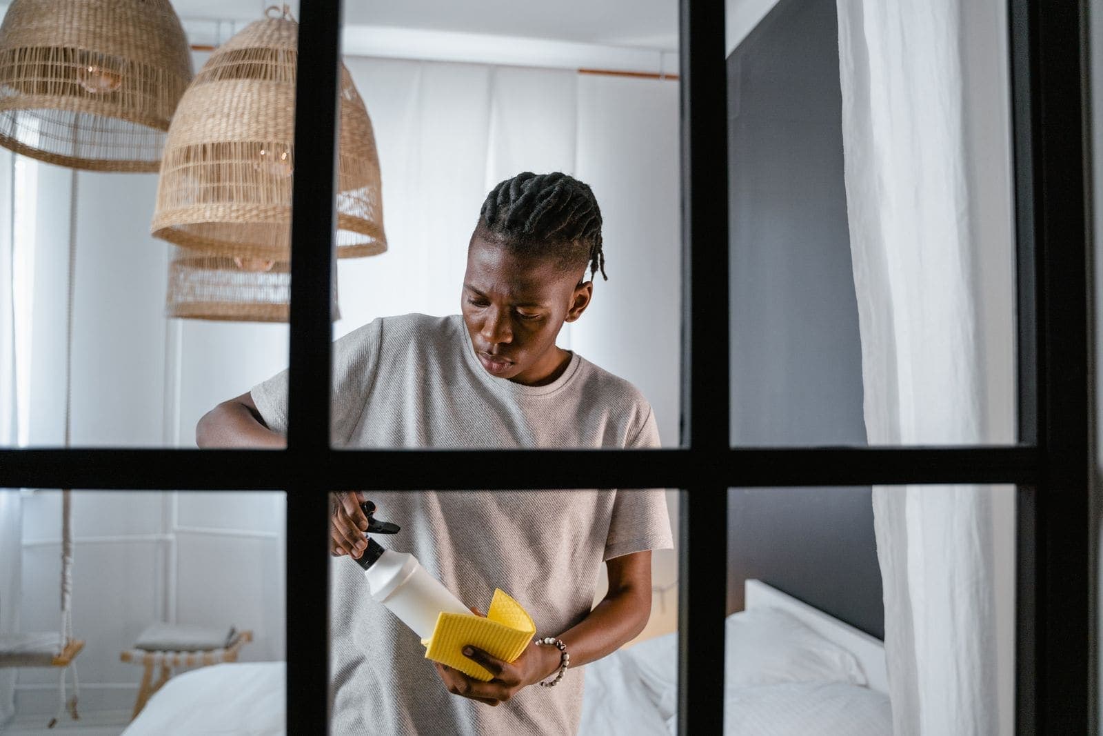 A young man cleaning with a spray bottle and a yellow sponge in a bright room