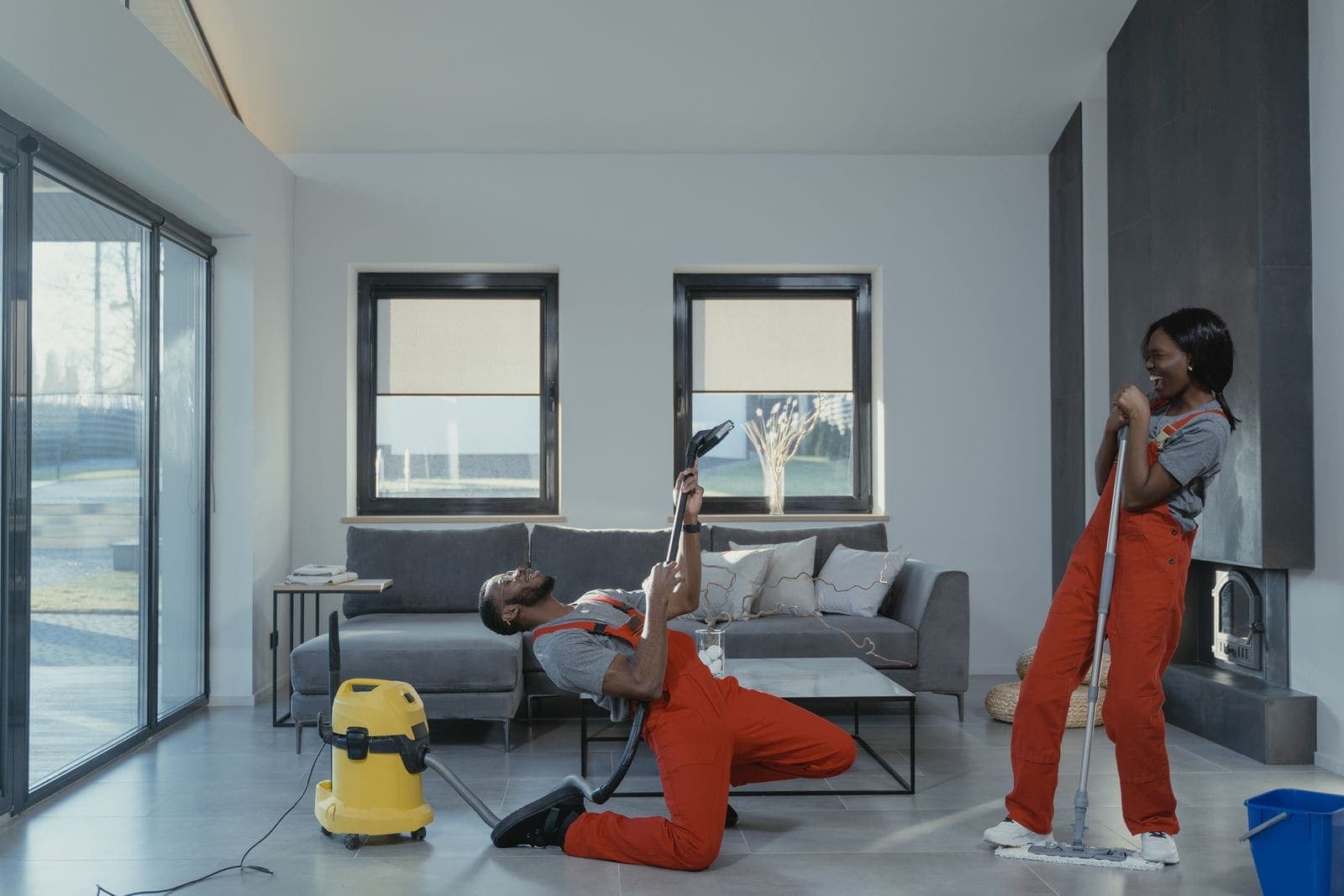 Two cleaners in red overalls having fun while they vacuum and mop a bright living room