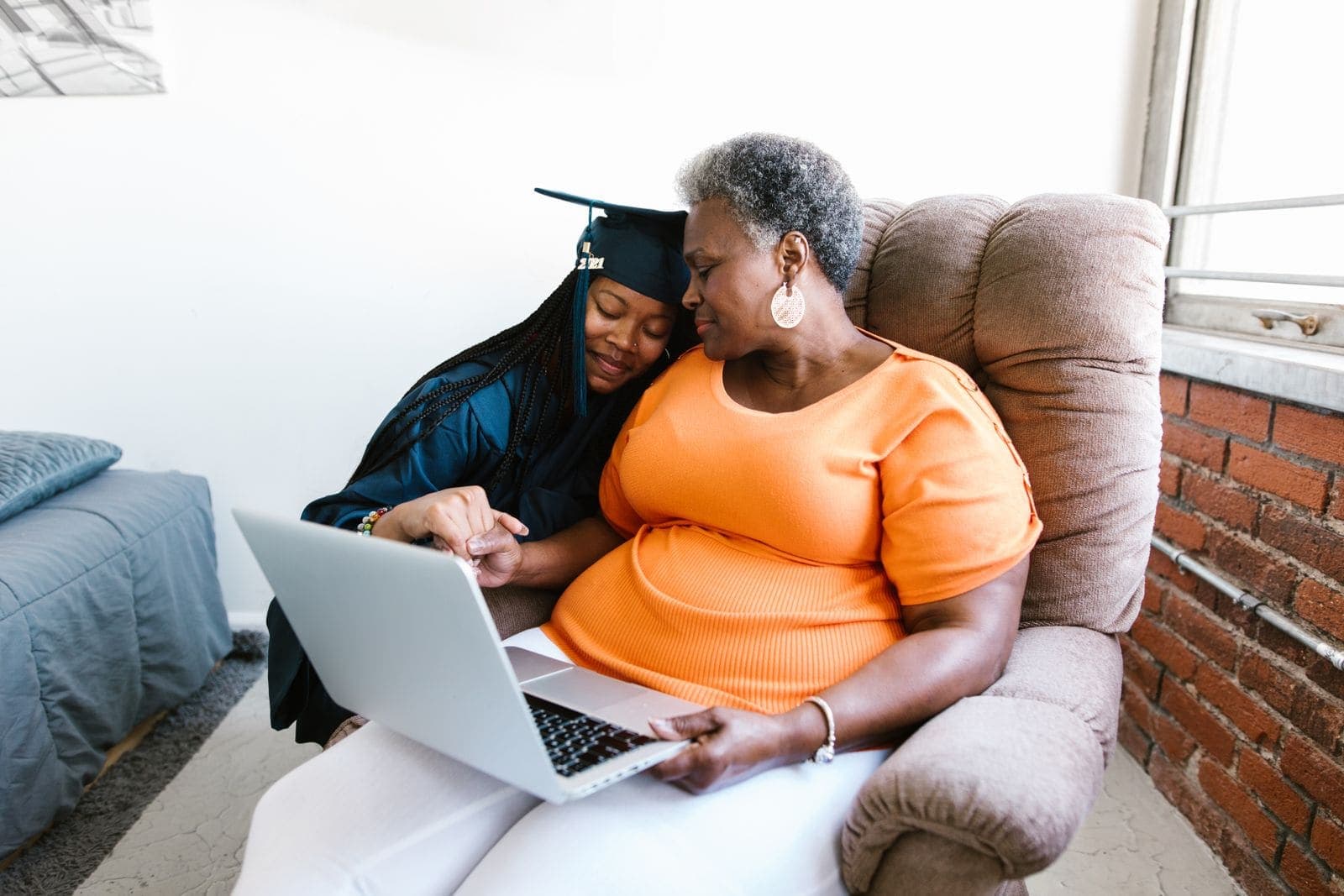 A young woman in a graduation gown hugging her grandmother in an armchair