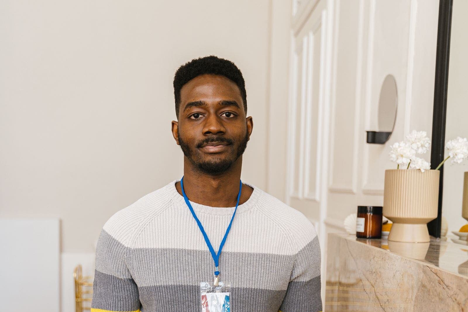 A young man wearing a lanyard, standing in a bright, tidy living room