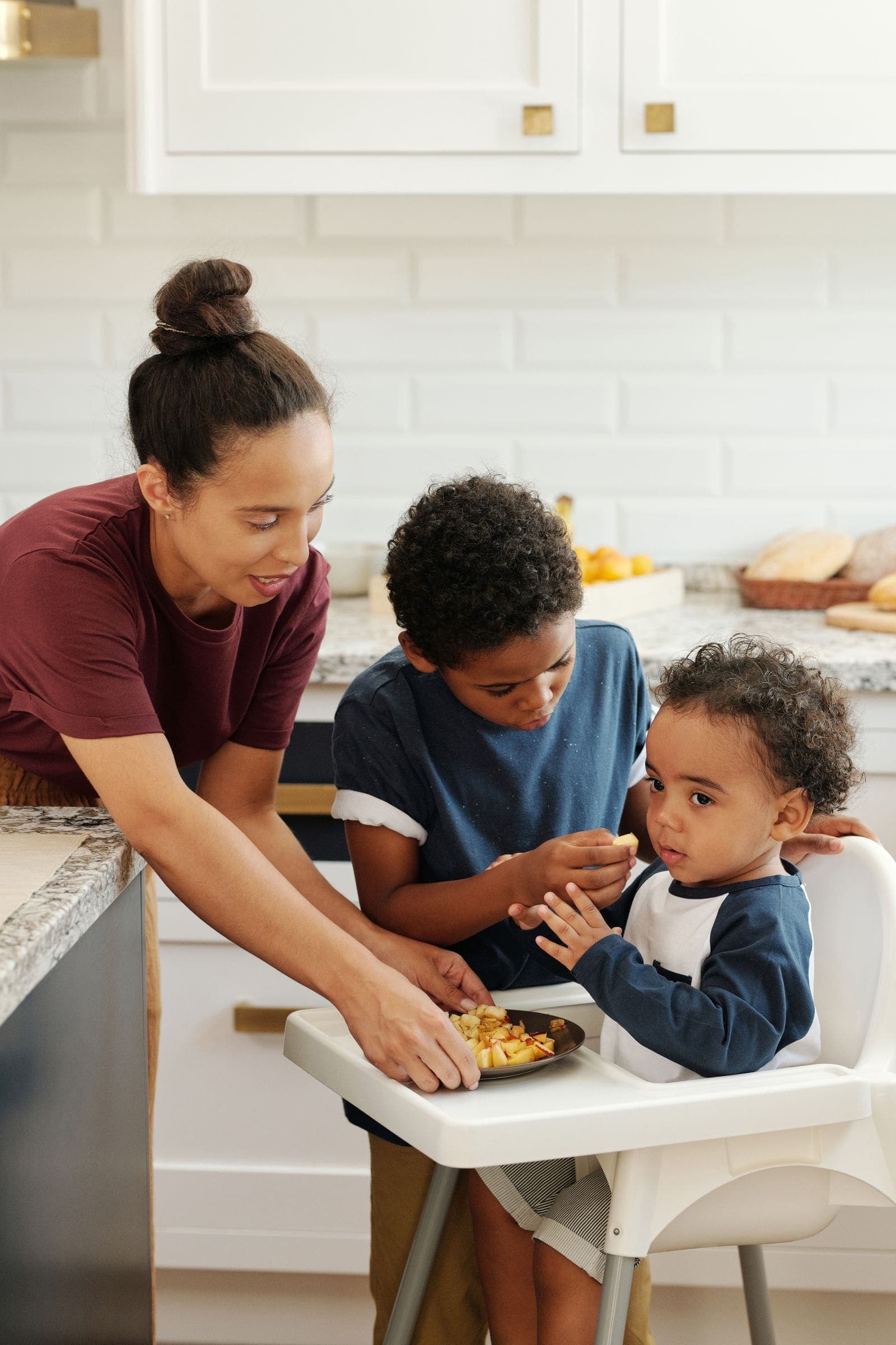 A mother sharing a snack with her two young sons in the kitchen