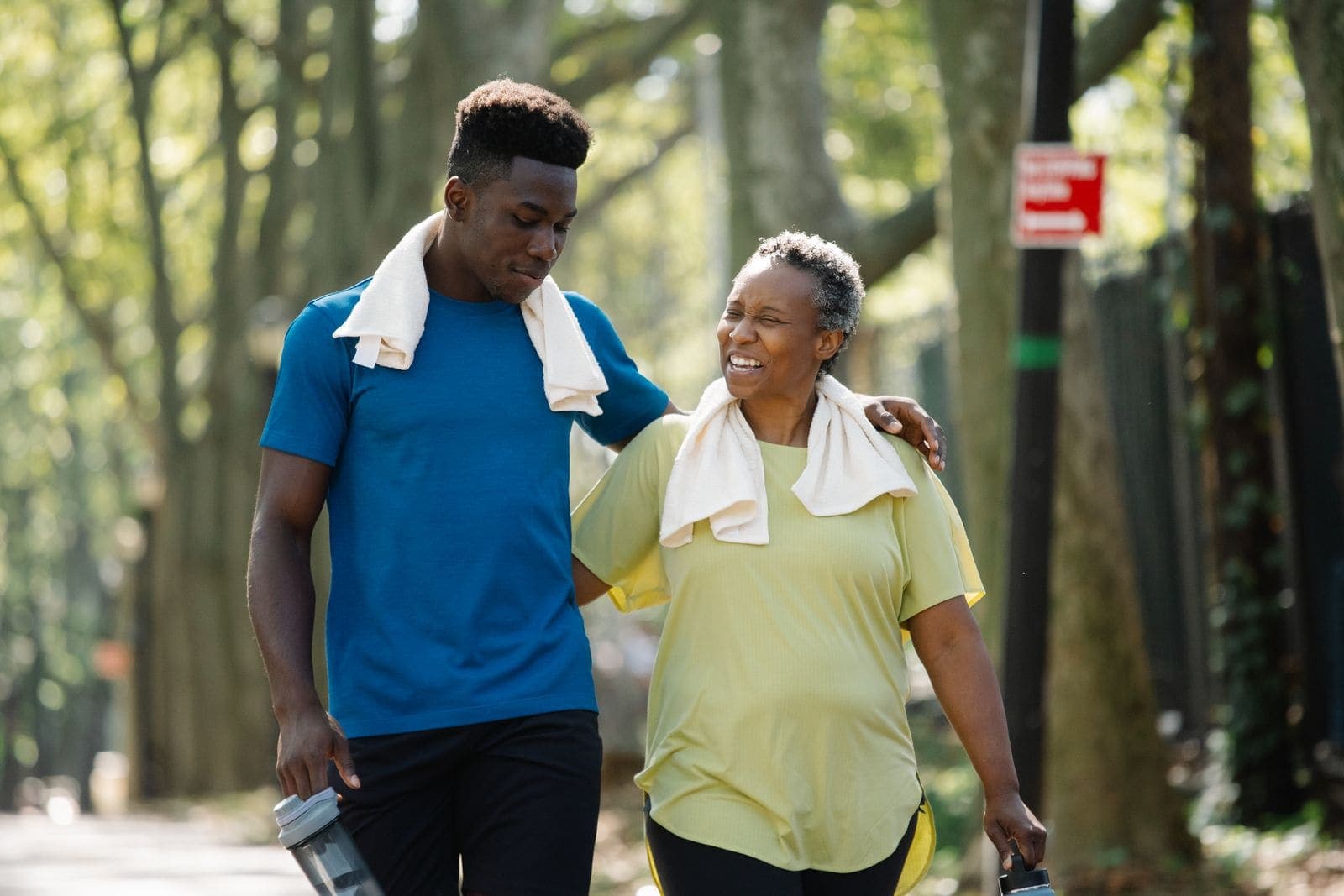 A young man walking arm in arm with a laughing older woman in a leafy park